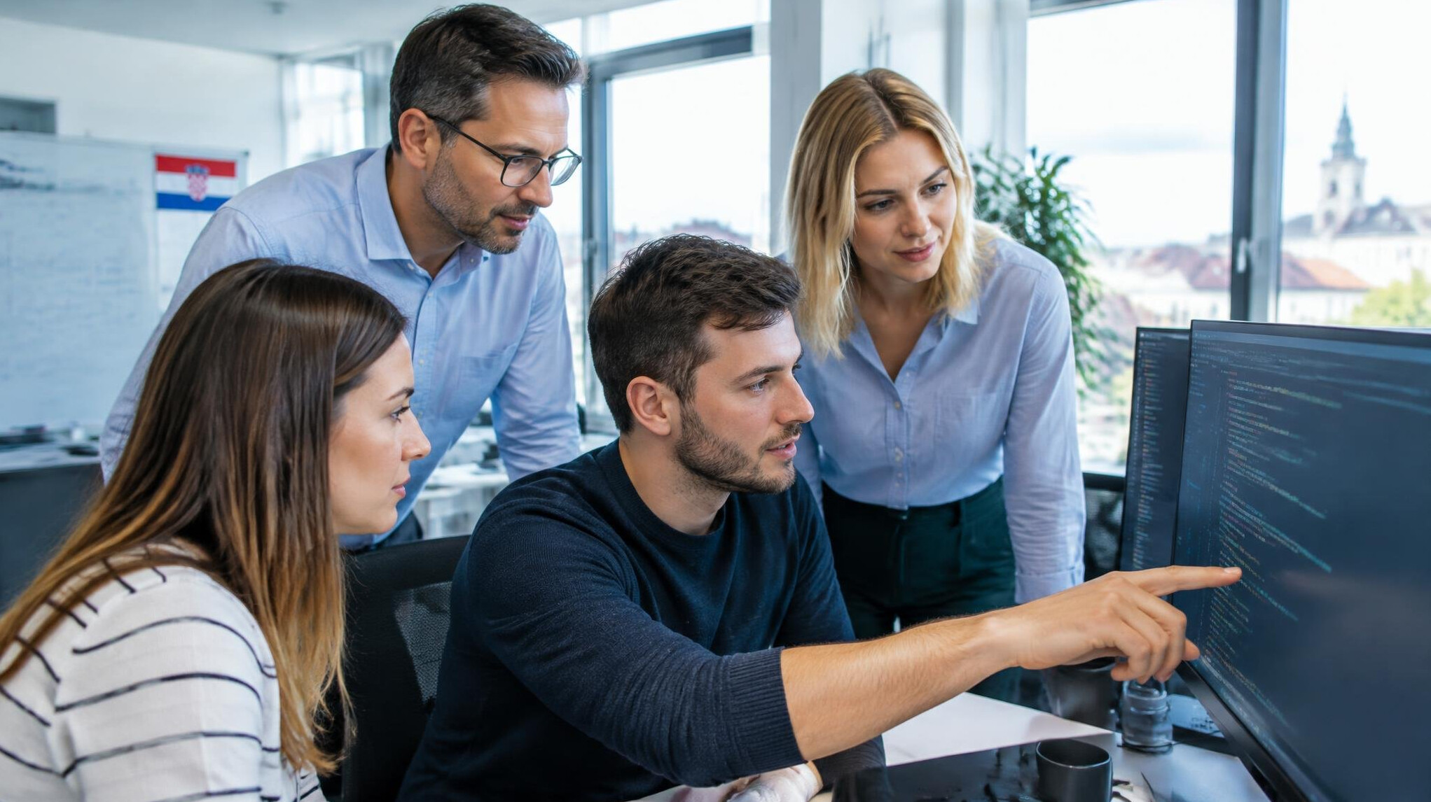 Diverse corporate team reviewing code together on a large monitor in a modern office